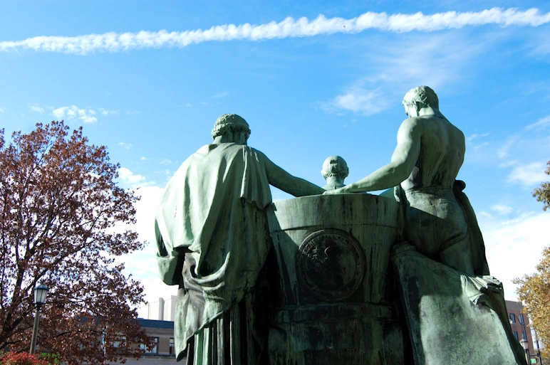  La parte de atrás de una estatua que recibe con los brazos abiertos a los estudiantes en una de las entradas del Quad.